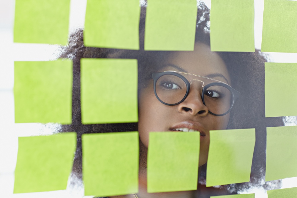 Portrait of a business woman with an afro behind sticky notes in bright glass office